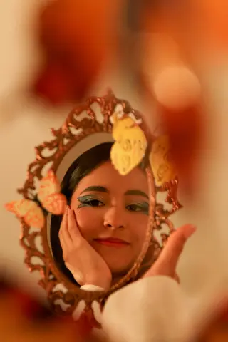 Young woman with blue eyeshadow reflected in an ornate vintage mirror amidst warm autumn leaves.