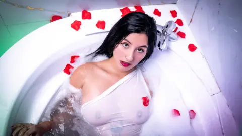 Young woman in a white top relaxing in a bubble bath surrounded by red rose petals for a romantic mood.