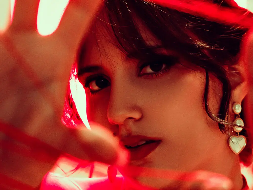 HaileyBellange looks toward the camera through a red-lit hand, showing her dark hair and pearl drop earrings.