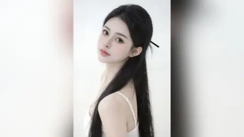AgelaHui poses looking over her shoulder with long black hair, wearing a white camisole against a plain white background.