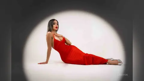 Elegant woman in a red satin evening gown posing gracefully against a soft spotlight background.