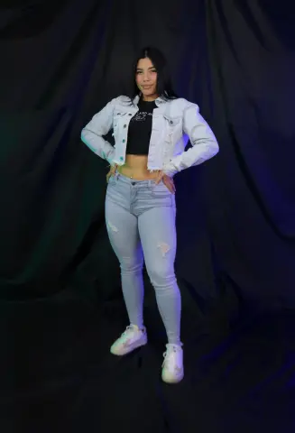 channeljonson — Young woman in light wash denim jacket and ripped skinny jeans posing against a dark studio backdrop.