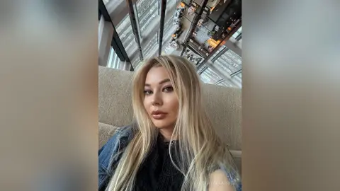 Blonde woman in a denim jacket relaxing in a modern high-rise building with a bright, airy mood.