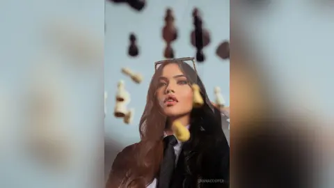 Elegant woman in a black blazer and tie posing amidst floating chess pieces in a surreal, dreamy atmosphere.