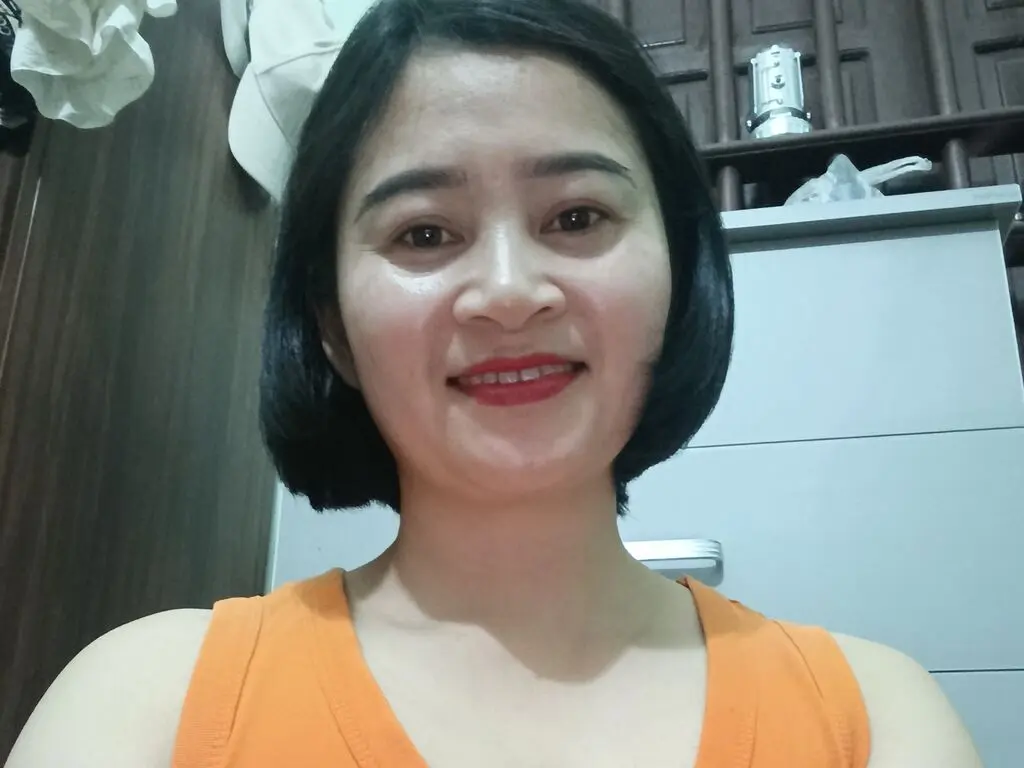 Smiling woman in an orange tank top posing indoors with a warm and friendly expression.