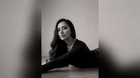 Elegant woman in a black long-sleeve top posing in a moody black and white studio portrait.