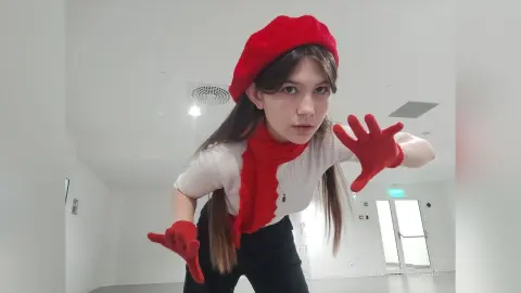Young woman in a red beret and red gloves posing playfully in a bright, minimalist white room.