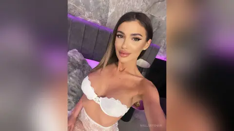 Glamorous woman in white lace lingerie posing in a modern room with purple ambient lighting.