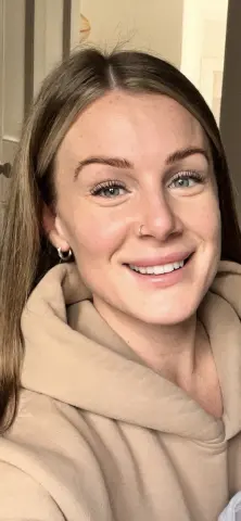 PixiePlayful_ox smiles at the camera, wearing a tan hoodie with her light brown hair down.