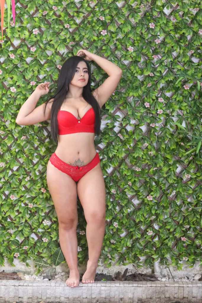 AgathaVegaa poses in red lace lingerie and stockings while leaning against a white door frame.