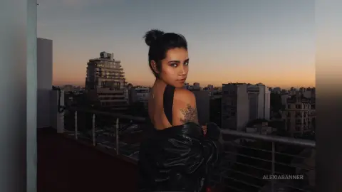 Young woman in a black leather jacket looking over her shoulder on a city rooftop at sunset.