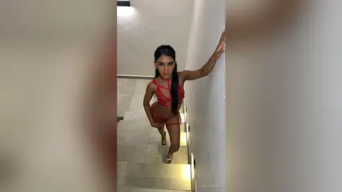 Elegant woman in a red lace bodysuit posing in a modern minimalist hallway with a moody atmosphere.