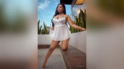 Elegant woman in a white lace mini dress posing on a sunny balcony with a confident mood.