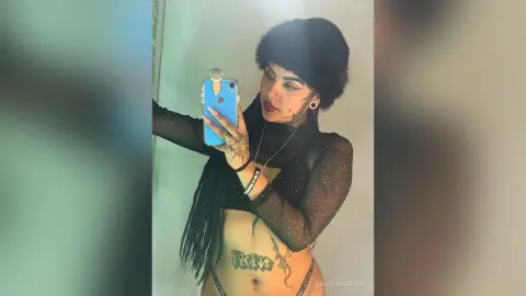 Stylish woman in a black sheer top and faux fur hat taking a confident mirror selfie indoors.