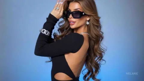 Stylish woman in a black cutout sweater and sunglasses posing against a blue studio background.