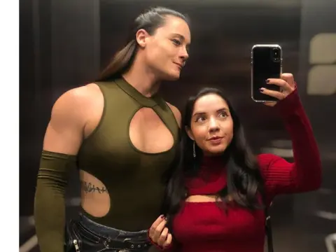 Two women in stylish outfits taking a selfie in a modern indoor setting with a confident mood.