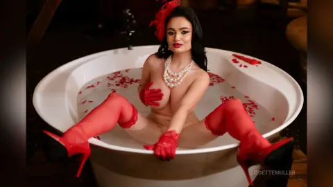 Glamorous woman in red gloves and stockings relaxing in a white bathtub surrounded by rose petals.