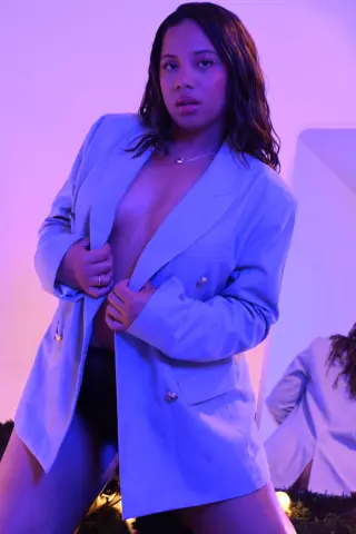 Fashionable woman in a light blue oversized blazer posing against a soft purple background with a moody vibe.