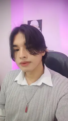 Young man with dark hair wearing a grey sweater and white collared shirt in a room with purple lighting.