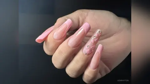 Close-up of long pink ombre coffin nails with glittery textured accents and small rhinestone decorations.