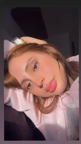 AbbyChannel poses close up wearing a pink hoodie with her hands behind her head, showing her long brown hair and face.