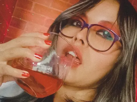 Young woman with glasses sipping a red drink in a moody, dimly lit setting.