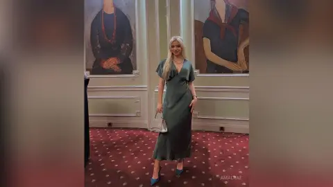 Elegant woman in a dark green satin maxi dress posing in a classic art gallery setting.