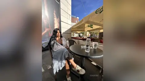 Young woman in a white blouse and grey skirt relaxing at an outdoor cafe with coffee on a sunny day.