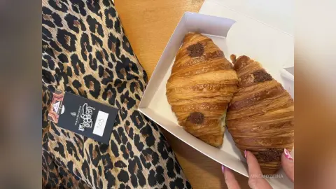 MnemoZeina displays two golden, flaky croissants in a white cardboard box resting on a leopard print fabric surface.
