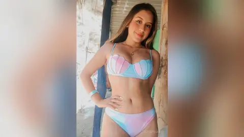 Smiling young woman in a pastel blue and pink bikini posing outdoors in bright summer sunlight.