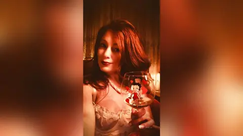 Elegant woman in a white lace camisole holding a wine glass in a warm, moody indoor setting.