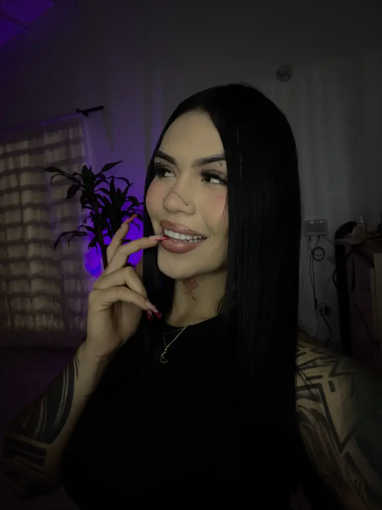 JulsWest has long black hair and wears black-rimmed glasses while looking directly at the camera in a close-up shot.