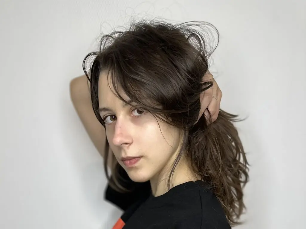 Young woman with messy brown hair wearing a black t-shirt against a plain white background.