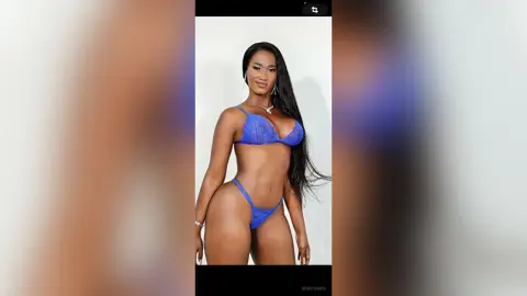 Confident Black woman in a blue lace bikini set posing against a white studio background.