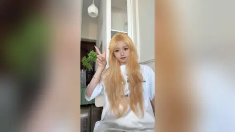 Blonde woman in a white t-shirt making a peace sign in a bright, minimalist modern room.