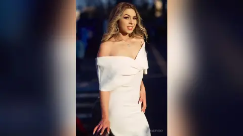 Smiling blonde woman in an elegant white off-the-shoulder evening gown posing outdoors in golden hour light.