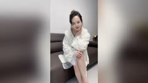 EnyaLin sits on a brown leather sofa wearing a white fluffy robe with lace trim.