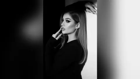 Elegant woman with long hair in a black outfit posing against a minimalist background in a moody black and white portrait.