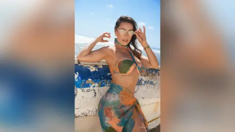 Smiling woman in a colorful patterned bikini and sarong posing on a sunny beach balcony.