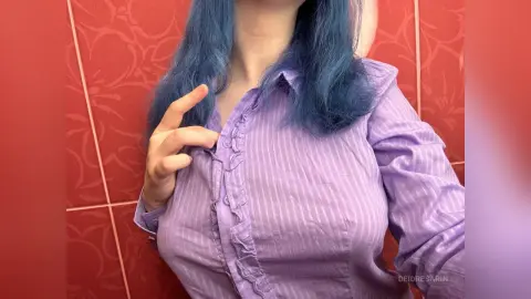 DeidreSarin wears a purple striped button-down shirt, showing her chest and blue hair against a red tiled wall.