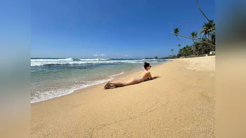Woman in bikini relaxing on a sunny sandy beach by the ocean waves under a clear blue sky.