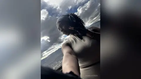 PamelaCreed wearing a light tan tank top and black headphones, posing against a cloudy blue sky.