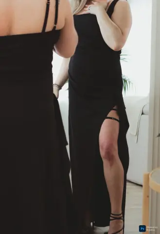 Elegant woman in a black evening gown with a high slit standing in a bright, modern living room.