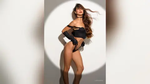 Glamorous woman in black lingerie and long gloves posing against a minimalist studio background.