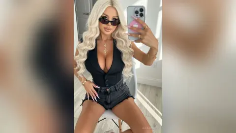 AlexaEvans poses in a black low-cut bodysuit and denim shorts, showing off her long blonde hair and sunglasses while taking a mirror selfie.