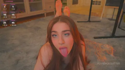 Young woman with long brown hair sticking her tongue out while relaxing on a grey shag rug in a cozy room.