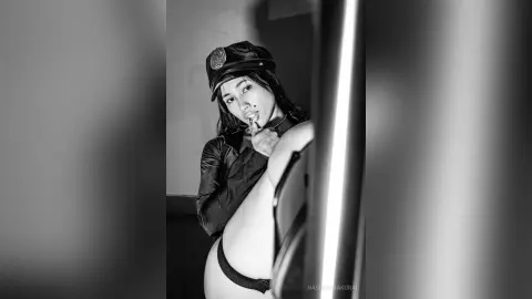 NashiroSakurai poses in a black police officer hat and uniform, looking toward the camera with a finger to her lips.