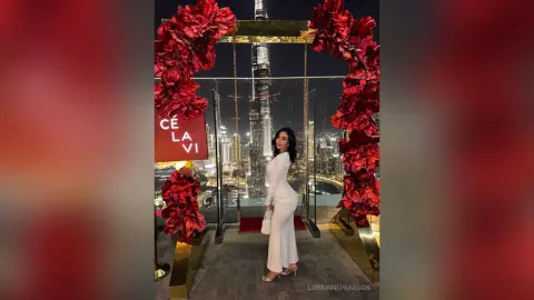 Elegant woman in a white evening gown posing by a floral arch at a rooftop lounge with Burj Khalifa view.