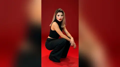 Young woman in a black sleeveless top and trousers posing against a vibrant red studio background.
