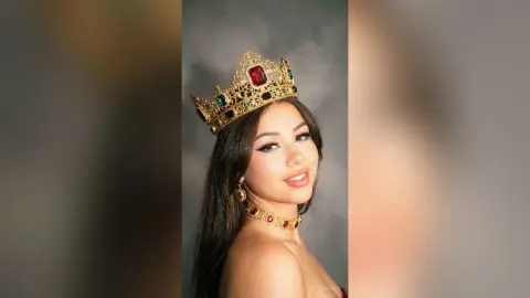 Elegant woman wearing a gold crown and ruby necklace against a moody grey background.